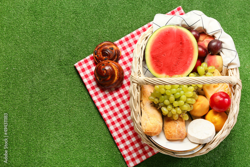 Wicker basket with tasty food for picnic on green background