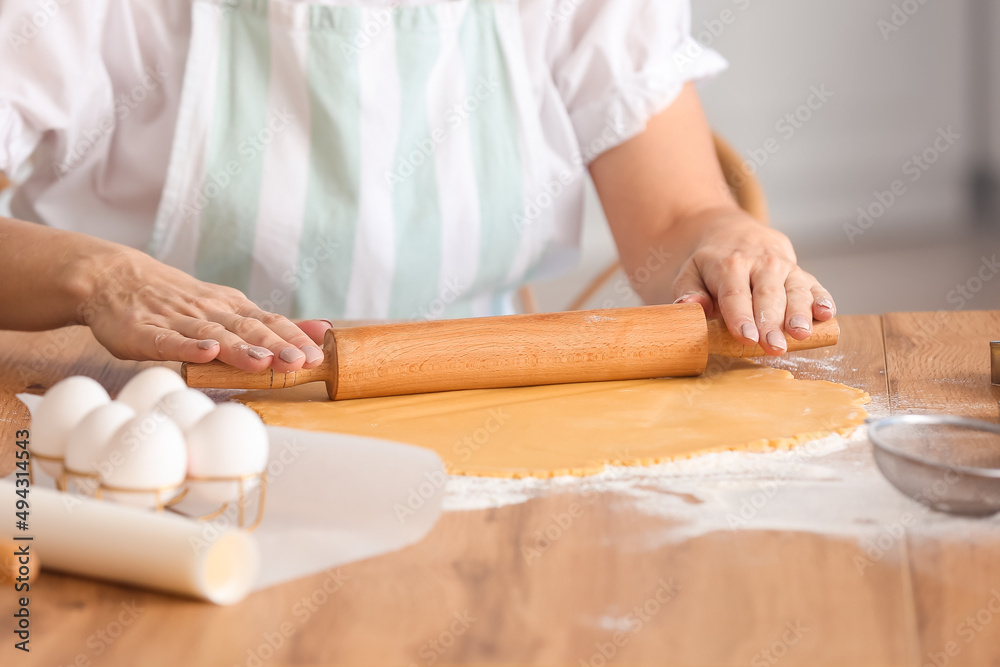 Mature woman rolling out dough for cookies at table in kitchen Mature woman rolling out dough for cookies at table in kitchen
