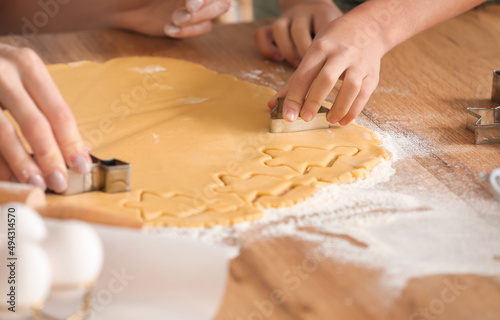 Mature woman cutting dough for cookies at table in kitchen, closeup