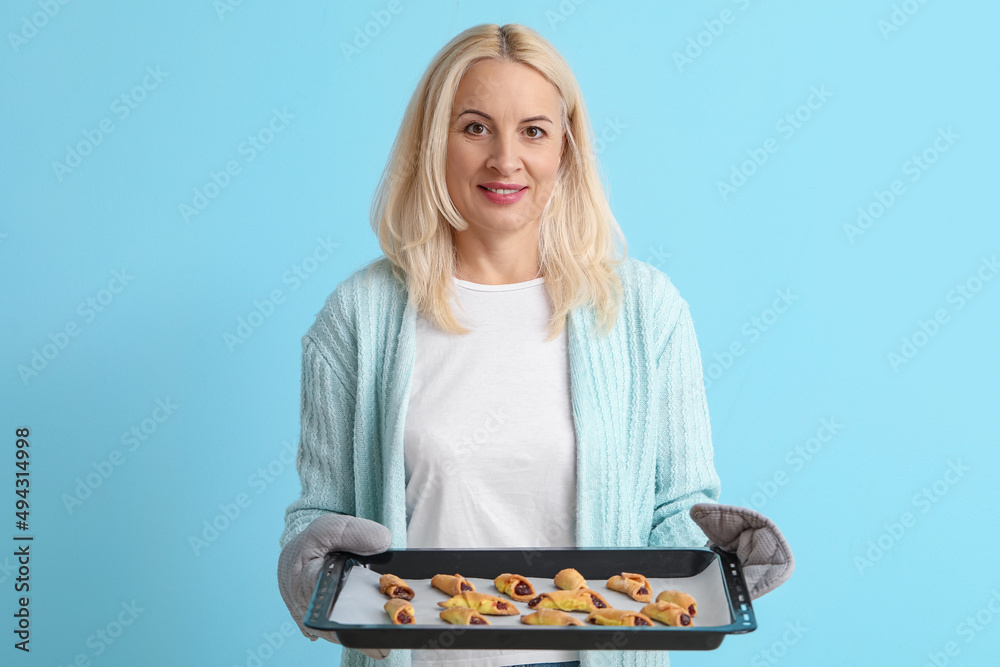 Mature woman holding baking dish with cookies on blue background Mature woman holding baking dish with cookies on blue background