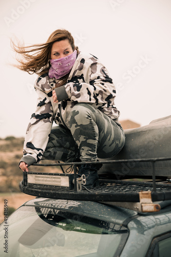 Woman on the top of a car wearing camouflage clothes and a violet bandana