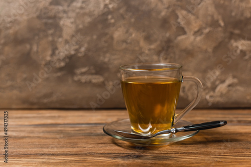 Cup of tea on saucer and spoon on wooden surface on textured stone background.