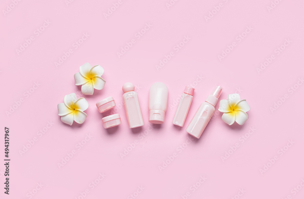 Travel bottles, jars with cosmetic products and flowers on pink background