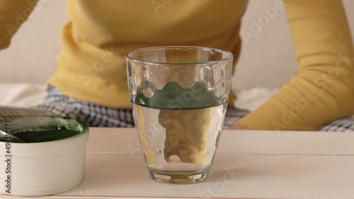 Girl putting a spoon of chlorella algae powder into a glass of water and stirring it