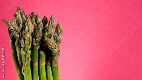 on the left, a bunch of fresh green asparagus stands on a pink background. side view. spring vitamins
