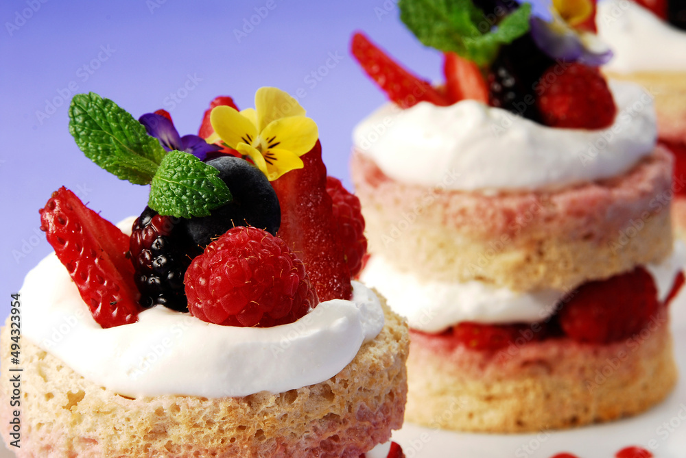 cake or sponge cake with red berries and edible flowers layered with whipped cream on lilac background, summer cake	
