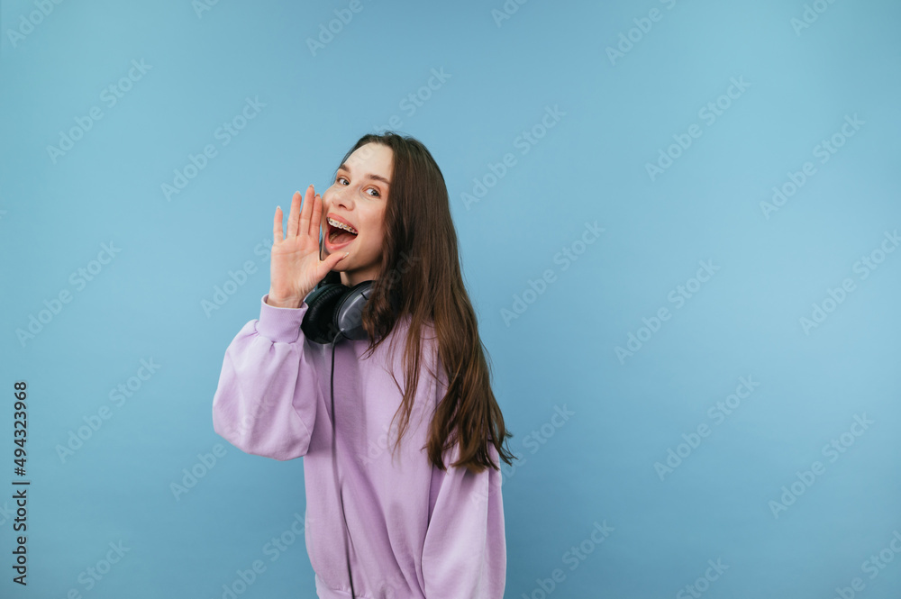 Positive woman in a purple sweatshirt stands against a blue background and looks at the camera with a smile on his face. Positive woman in a purple sweatshirt stands against a blue background and looks at the camera with a smile on his face.