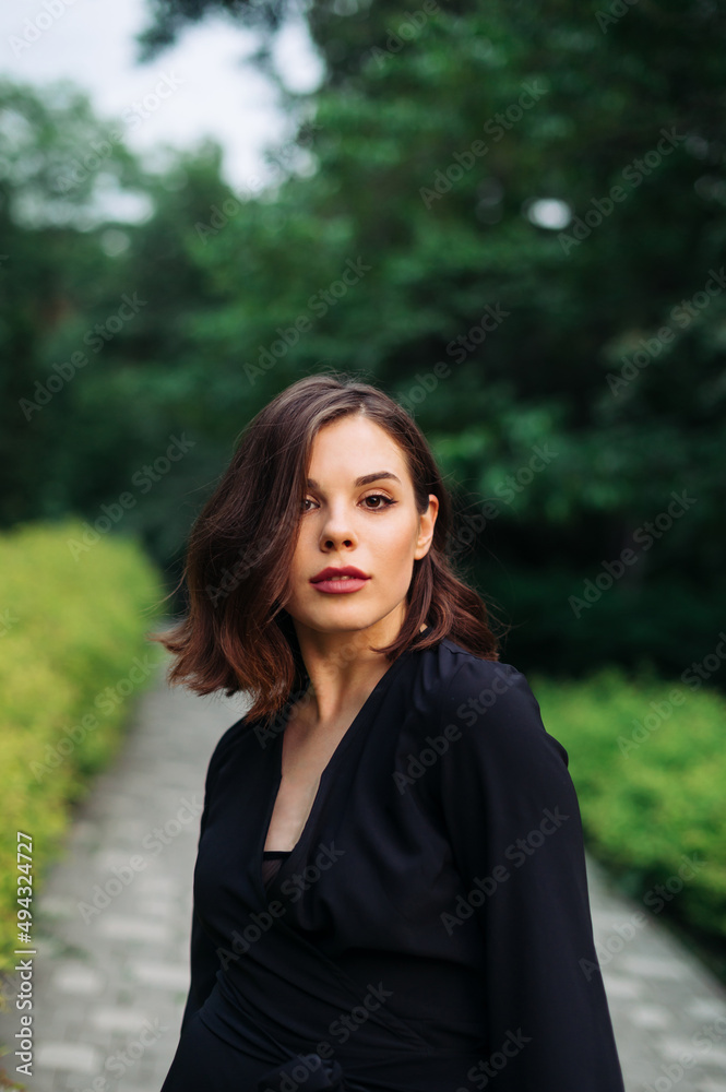 Portrait of a beautiful young woman in black clothes on a walk in the park, looking at the camera with a serious face. Portrait of a beautiful young woman in black clothes on a walk in the park, looking at the camera with a serious face.