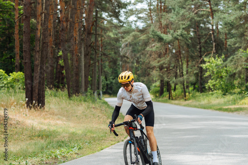 Man in outfit trains on a bicycle in the woods on an asphalt road, quickly rides forward,