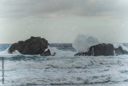Beautiful ocean view with large powerful waves splashing on the rocks. Cloudy sky.