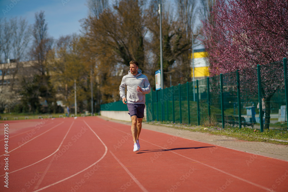 Obraz premium A man in a gray hoodie is jogging at a sports stadium.