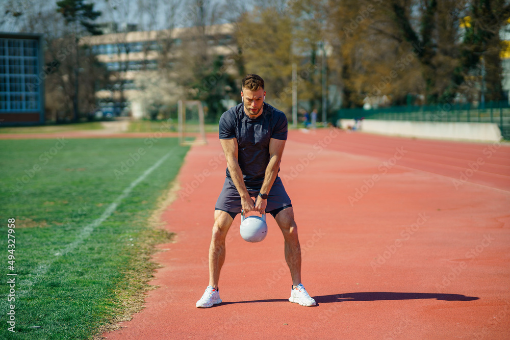 Young muscular man doing exercises with kettlebell outdoor. Weightlifting workout. Sports, fitness concept.