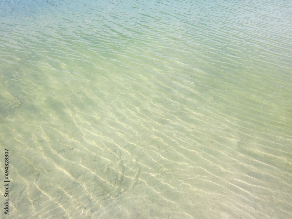 Shallow waves on the beach with translucent clean sand, in green-yellow tones. A ripple of waves with transparent reflexes and shadows