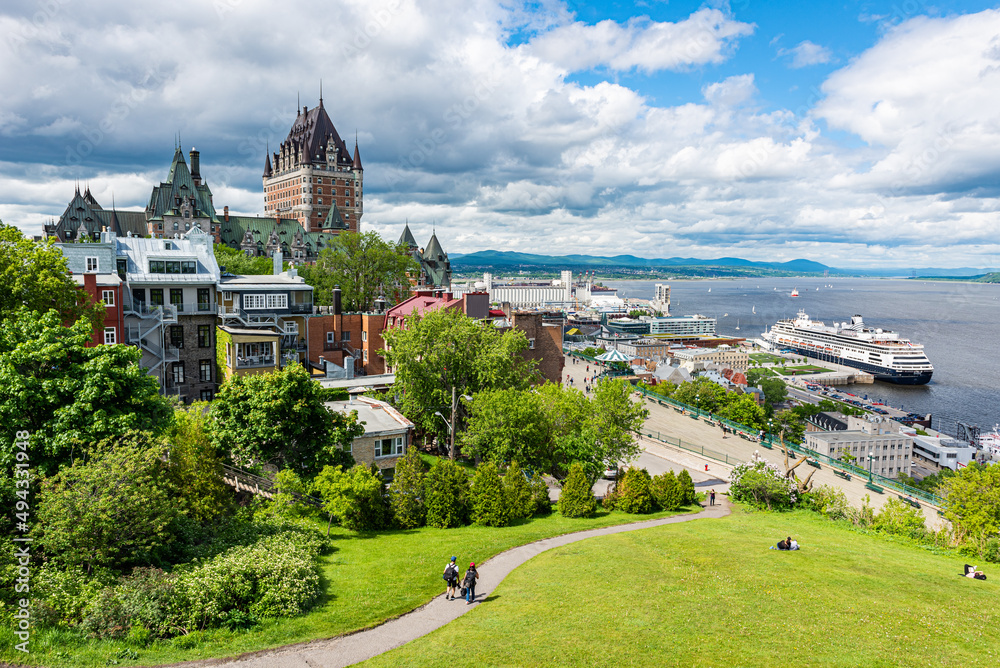 Obraz premium The frontenac castle and the St. Lawrence river with a cruise ship at the harbor in the Quebec city under a stormy sky at the beginning of the summer.