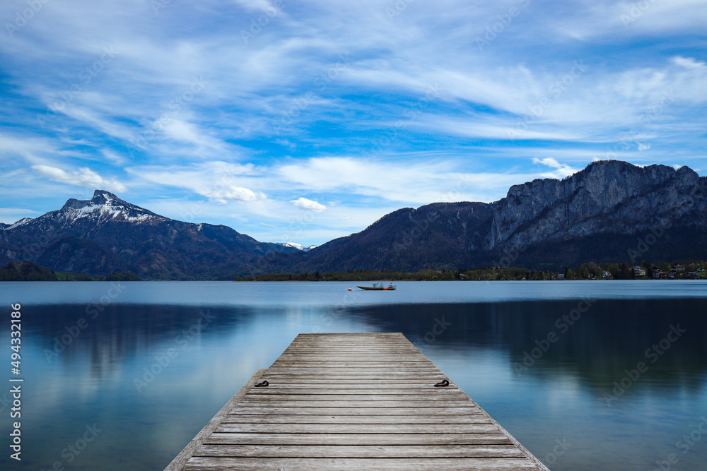Beautiful landscape view of a wooden pier on the lake against mountains and blue cloudy sky