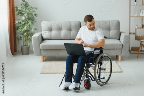 Portrait of smiling disabled male sitting in wheelchair and working on laptop from home. Young worker with special needs. Freelancer and people with disabilities concept.