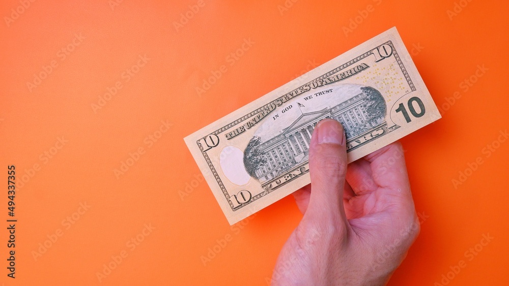 Man's hand is making a payment. Business Investment Economy Saving Loan Income Money and Finance concept. Male hand showing dollar cash on an orange background. Ten Dollar 10 USD. Prosperity concept.