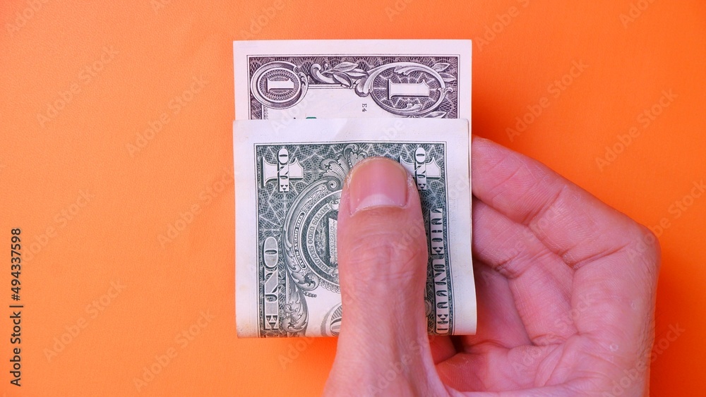 Man's hand is making a payment. Business Investment Economy Saving Loan Income Money and Finance concept. Male hand showing dollar cash on an orange background. One Dollar 1 USD. Prosperity concept. Man's hand is making a payment. Business Investment Economy Saving Loan Income Money and Finance concept. Male hand showing dollar cash on an orange background. One Dollar 1 USD. Prosperity concept.