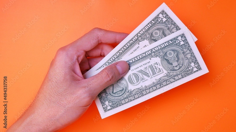 Man's hand is making a payment. Business Investment Economy Saving Loan Income Money and Finance concept. Male hand showing dollar cash on an orange background. One Dollar 1 USD. Prosperity concept. Man's hand is making a payment. Business Investment Economy Saving Loan Income Money and Finance concept. Male hand showing dollar cash on an orange background. One Dollar 1 USD. Prosperity concept.