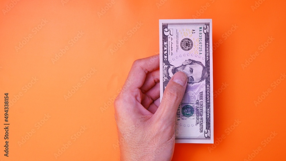 Man's hand is making a payment. Business Investment Economy Saving Loan Income Money and Finance concept. Male hand showing dollar cash on an orange background. Five Dollar 5 USD. Prosperity concept. Man's hand is making a payment. Business Investment Economy Saving Loan Income Money and Finance concept. Male hand showing dollar cash on an orange background. Five Dollar 5 USD. Prosperity concept.