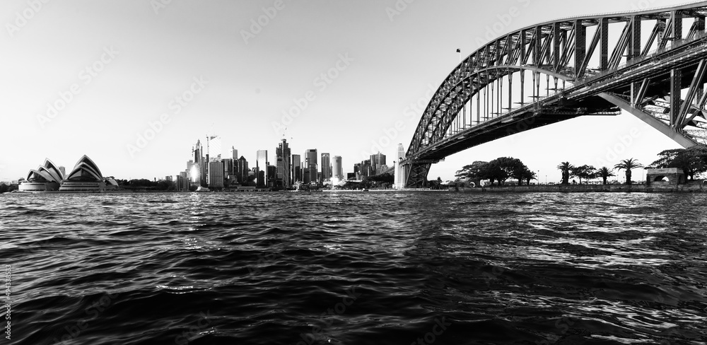 Naklejka premium Black and white shot of the Sydney Harbour Bridge with the cityscape against a cloudless sky