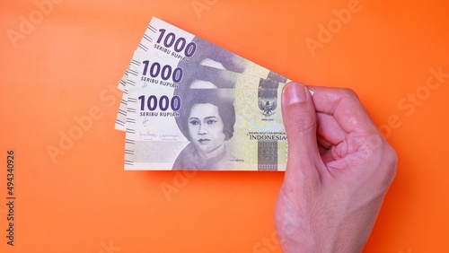 Indonesian Rupiah the official currency of Indonesia. Man's hand is making a payment. Male hand showing Indonesian Rupiah note. Business Investment Economy and Finance concept. Uang 1000 1.000 Rupiah.