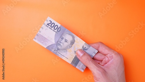 Indonesian Rupiah the official currency of Indonesia. Man's hand is making a payment. Male hand showing Indonesian Rupiah note. Business Investment Economy and Finance concept. Uang 2000 2.000 Rupiah