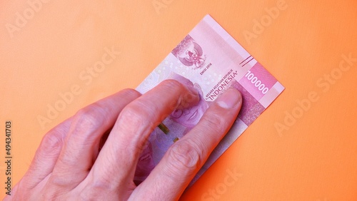 Indonesian Rupiah the official currency of Indonesia. Man's hand is making a payment. Male hand showing Indonesian Rupiah note. Business Investment Economy Loan and Finance concept Uang 100.000 Rupiah
