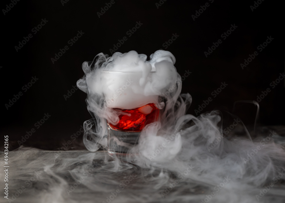 Bebida roja con hielo seco sobre fondo negro y con base de piedra. reacción  química con Humo saliendo abundantemente Stock Photo