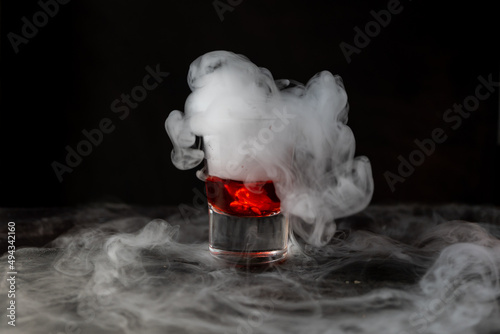 Bebida roja con hielo seco sobre fondo negro y con base de piedra. reacción química con Humo saliendo abundantemente photo