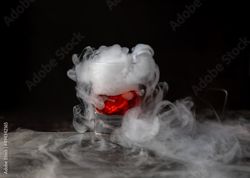 Bebida roja con hielo seco sobre fondo negro y con base de piedra. reacción química con Humo saliendo abundantemente