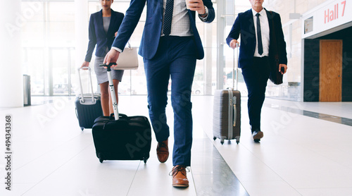 Our business requires us to travel. Cropped shot of three unrecognizable businesspeople walking and pulling suitcases while in the office during the day.