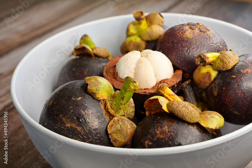 Open mangosteen (Garcinia mangostana) fruit and ripe whole fruits in a white bowl photo