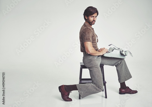 70s fashion. Studio shot of a 70s style businessman sitting on a stool using a typewriter.