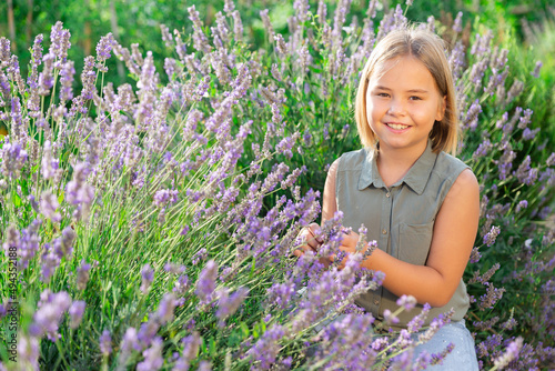Little girl in hat squatting beside lavender shrub in garden