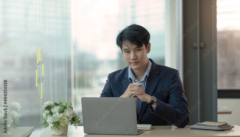 Charming Asian man working at the office using a laptop Looking at the camera. Charming Asian man working at the office using a laptop Looking at the camera.