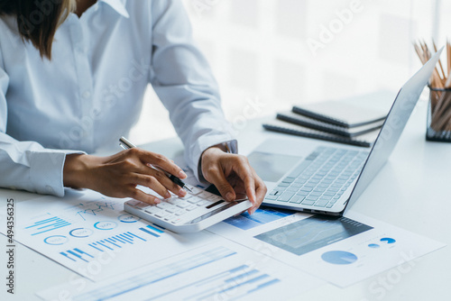 Asian woman is pointing at the report graph and has laptop on the front. Maybe preparing data for marketing report. window light