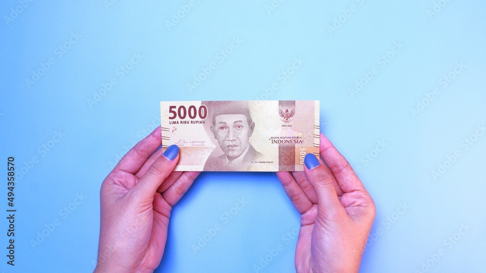 Indonesian Rupiah the official currency of Indonesia. woman's hand is making a payment. Female hand showing Indonesian Rupiah note. Business Investment Economy and Finance concept. Uang 5000 Rupiah. Indonesian Rupiah the official currency of Indonesia. woman's hand is making a payment. Female hand showing Indonesian Rupiah note. Business Investment Economy and Finance concept. Uang 5000 Rupiah.