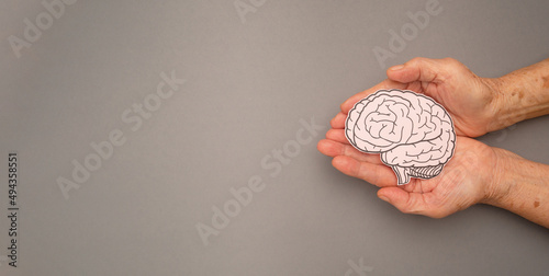 Brain shape made from paper on a palm senior woman on a gray background