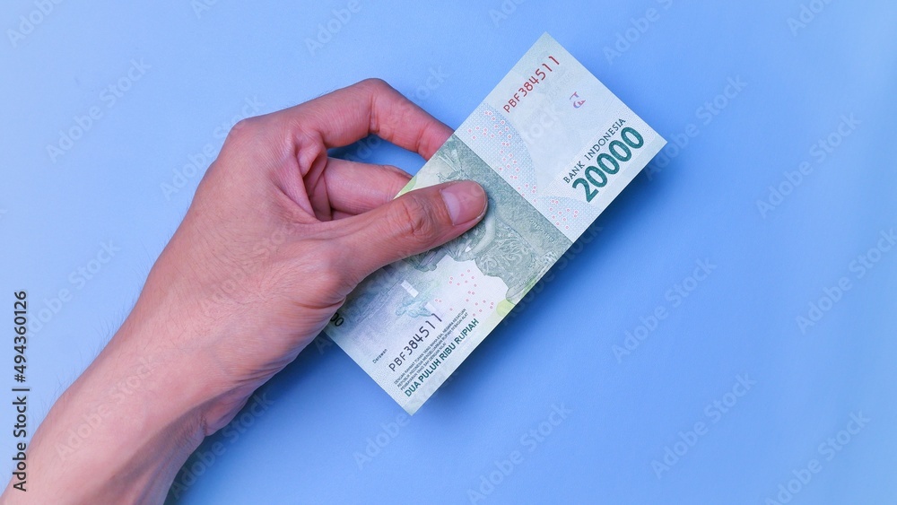 Indonesian Rupiah the official currency of Indonesia. Man's hand is making a payment. Male hand showing Indonesian Rupiah note. Business Investment Economy and Finance concept. Uang 20000 Rupiah. Indonesian Rupiah the official currency of Indonesia. Man's hand is making a payment. Male hand showing Indonesian Rupiah note. Business Investment Economy and Finance concept. Uang 20000 Rupiah.