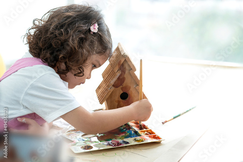 Photos Cute little girl mixes colors to paint a wooden birdhouse in her room, education