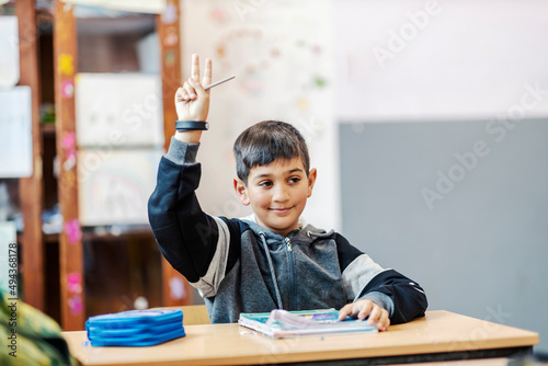 A smart Roma pupil rising hand for a right answer while sitting in classroom.