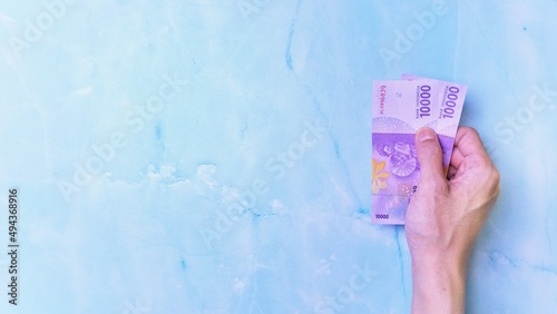 Indonesian Rupiah the official currency of Indonesia. Man's hand is making a payment. Male hand showing Indonesian Rupiah note. Business Investment Economy and Finance concept Uang 10000 10.000 Rupiah