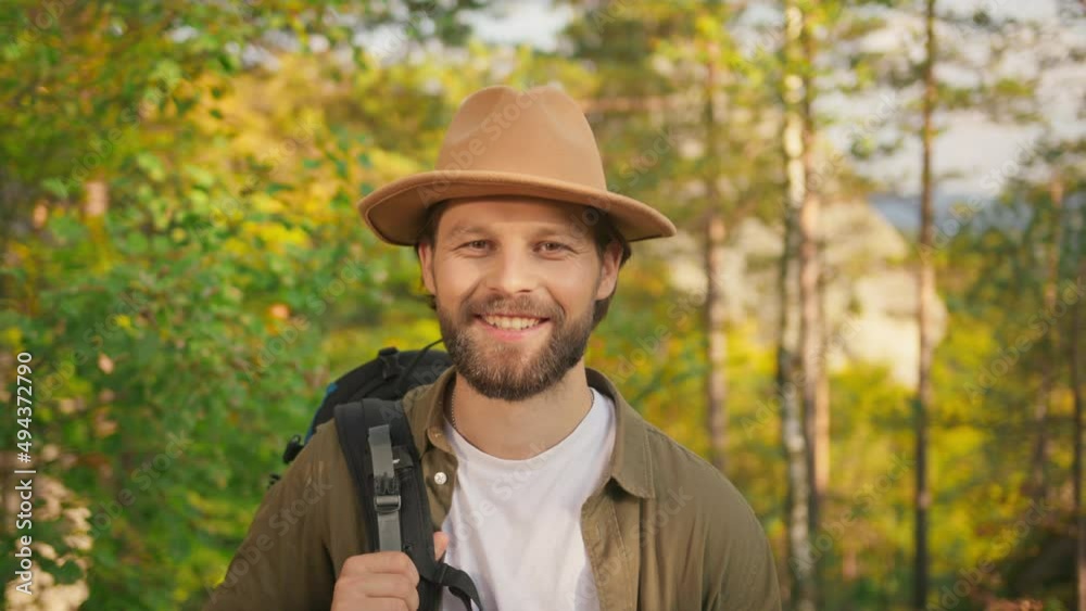 Outside portrait closeup handsome caucasian man bearded tourist with hat backpack rucksack smiling cheerful at camera. Wild forest background. Summertime. Tourism. Outside portrait closeup handsome caucasian man bearded tourist with hat backpack rucksack smiling cheerful at camera. Wild forest background. Summertime. Tourism.