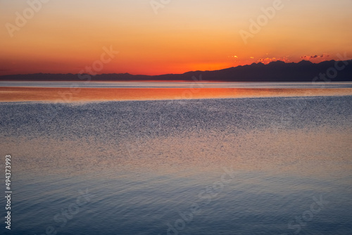 Beautiful sunset on mountain lake with mountain ridge silhouette. Colorful sunrise with orange sky on Issyk-kol lake. Travel  tourism in Kyrgyzstan concept.