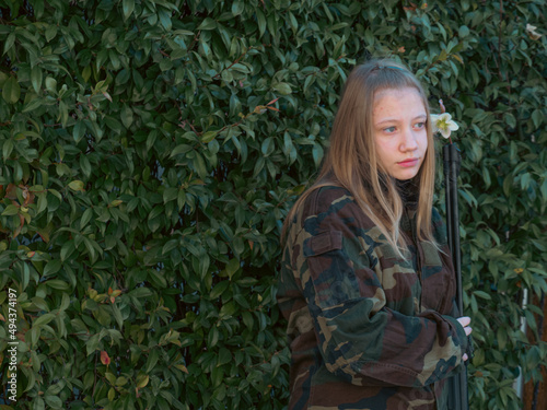 caucasian blond teen aged soldier girl  on a checkpoint holding a rifle gun and wearing a camo green military uniform during a conflict in a war zone photo