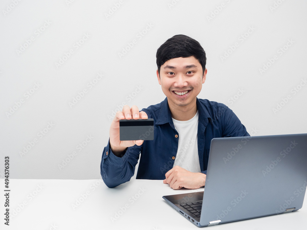 Man happy emotion smiling holding credit card and sit at the desk with laptop Man happy emotion smiling holding credit card and sit at the desk with laptop