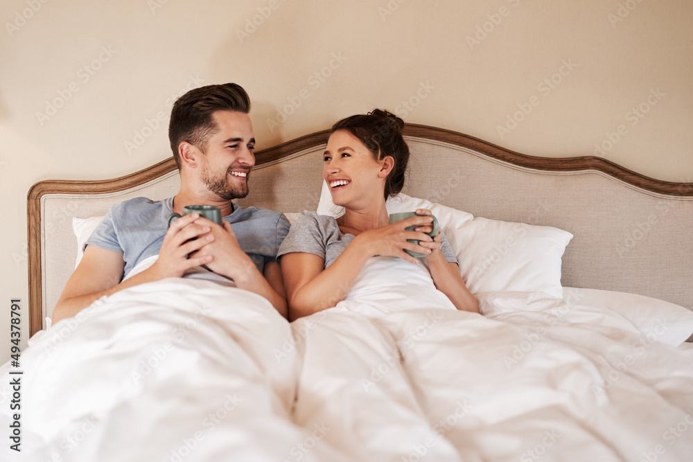 Fototapeta premium Starting off our morning on a warm note. Shot of a happy young couple drinking coffee in bed in their bedroom at home.