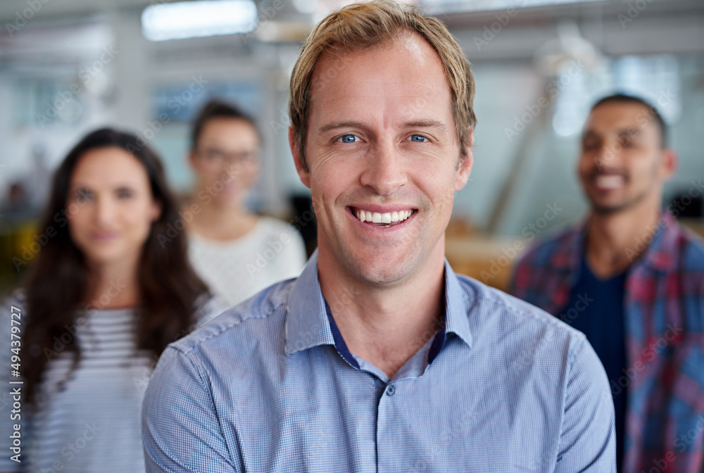 Leading with positive motivation. Handsome man smiling at the camera with staff in the background. Leading with positive motivation. Handsome man smiling at the camera with staff in the background.