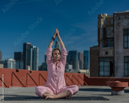 Young blonde woman in pink coveralls and barefoot practices yoga on a downtown Los Angeles Roof top with the LA skyline behind her photo